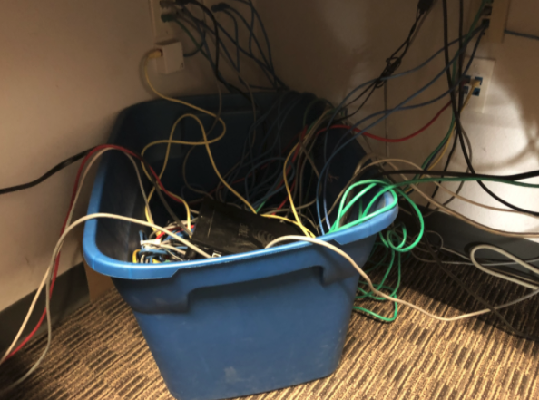 Messy computer cords and wiires under a desk.